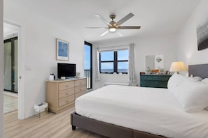 Ein Schlafzimmer mit einem Bett, einer Kommode, einem Fernseher, einem Deckenventilator, einem Fenster mit Ausblick und einer Kommode mit Dekoration.