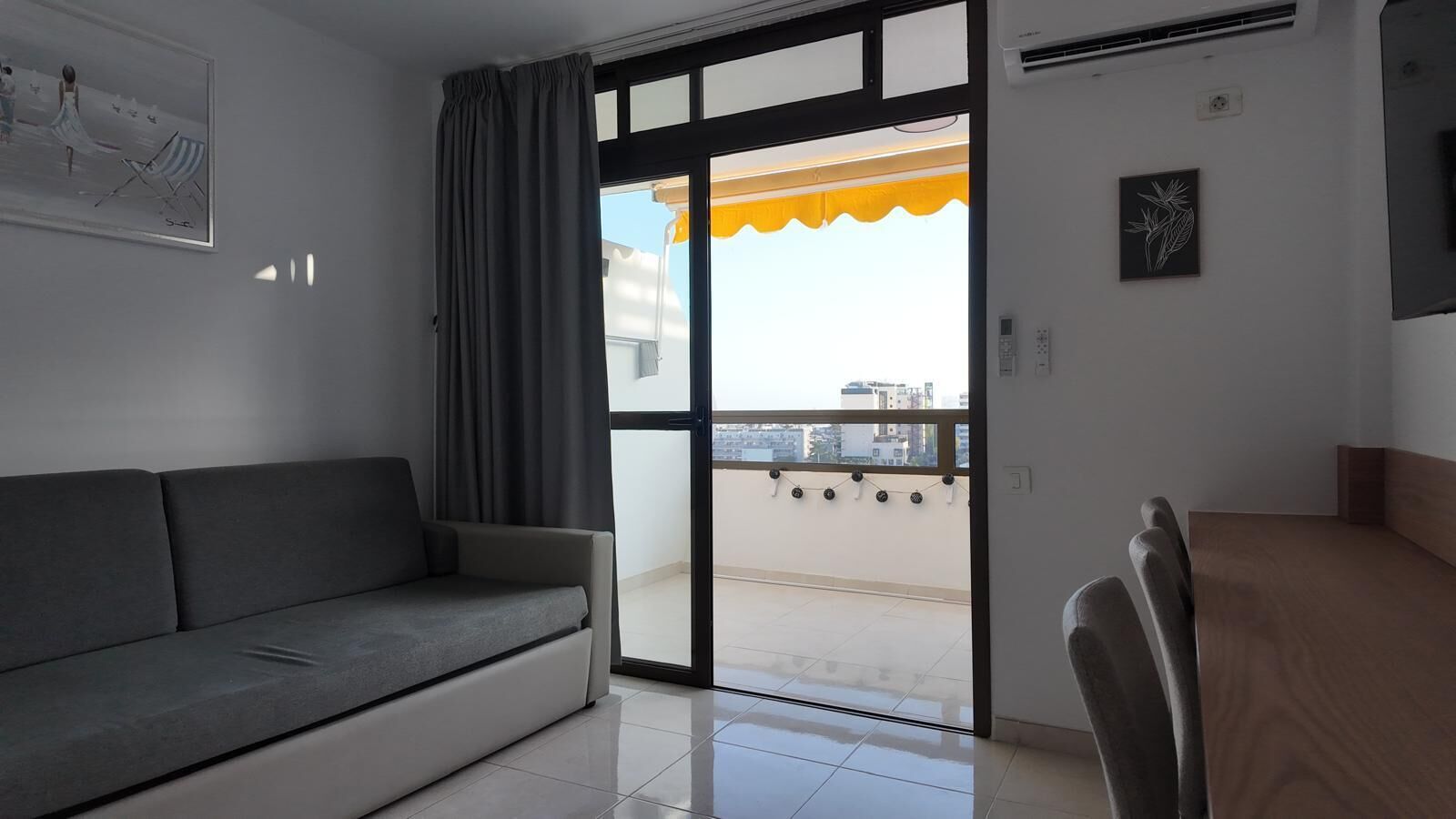 A room with a sofa, a dining table, and a sliding glass door leading to a balcony.
