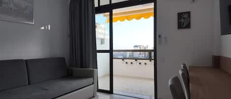 Quarto com sofá, mesa de jantar e porta de vidro deslizante que dá para uma varanda.