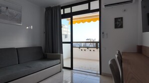 A room with a sofa, a dining table, and a sliding glass door leading to a balcony. - Maspalomas Dunes Ocean View Pool Apartment (Maspalomas)