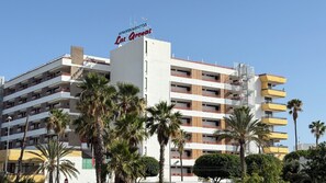 Ein mehrstöckiges Hotel mit Balkonen, Palmen und einem Schild mit der Aufschrift 'Apartamentos Carreiras'.