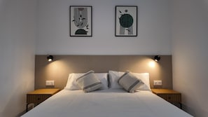 Ein ordentlich bezogenes Bett mit zwei Kissen, einem Kopfteil und zwei Nachttischen mit Lampen.