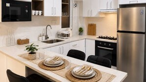 A modern kitchen with white cabinets, a stainless steel refrigerator, a microwave, and a gas stove.