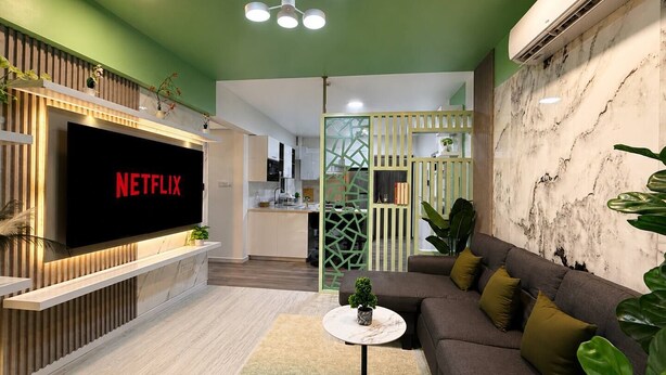 A modern living room with a flat-screen TV, a sofa, a coffee table, and a kitchen in the background.