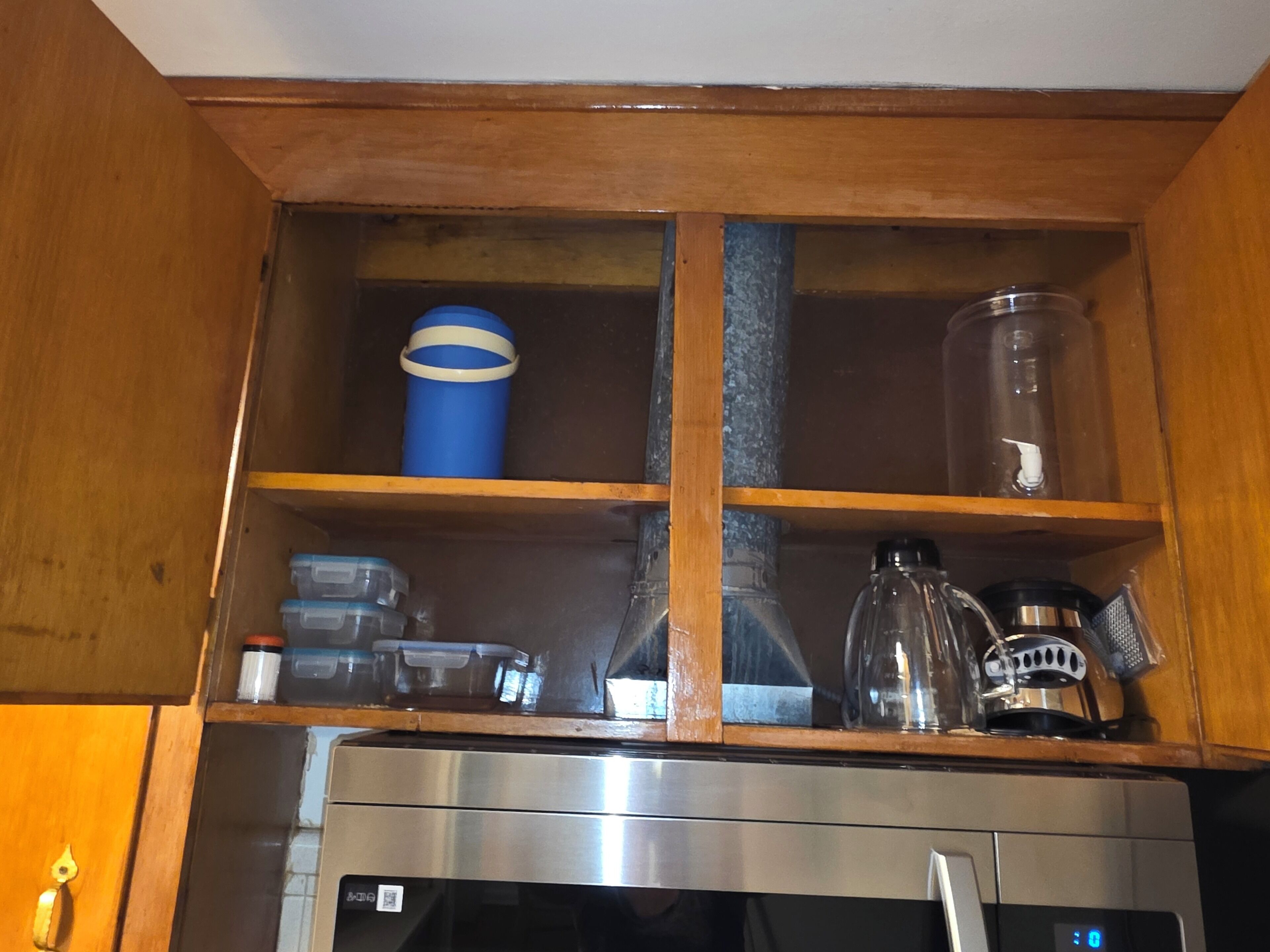 A kitchen with a stainless steel refrigerator, wooden cabinets, and a built-in shelf with various containers and kitchenware.