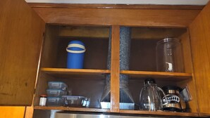 A kitchen with a stainless steel refrigerator, wooden cabinets, and a built-in shelf with various containers and kitchenware.