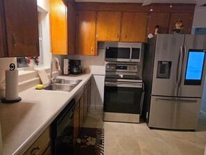 Una cucina con mobili in legno, elettrodomestici in acciaio inossidabile tra cui forno a microonde, forno e frigorifero, una macchina da caffè e una finestra con vista sulle viti.