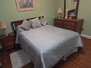 A bedroom with a bed, a nightstand, a dresser, a mirror, and a framed picture on the wall.