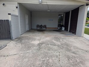 A covered outdoor area with a concrete floor, a gated entrance, two chairs, and a small table.