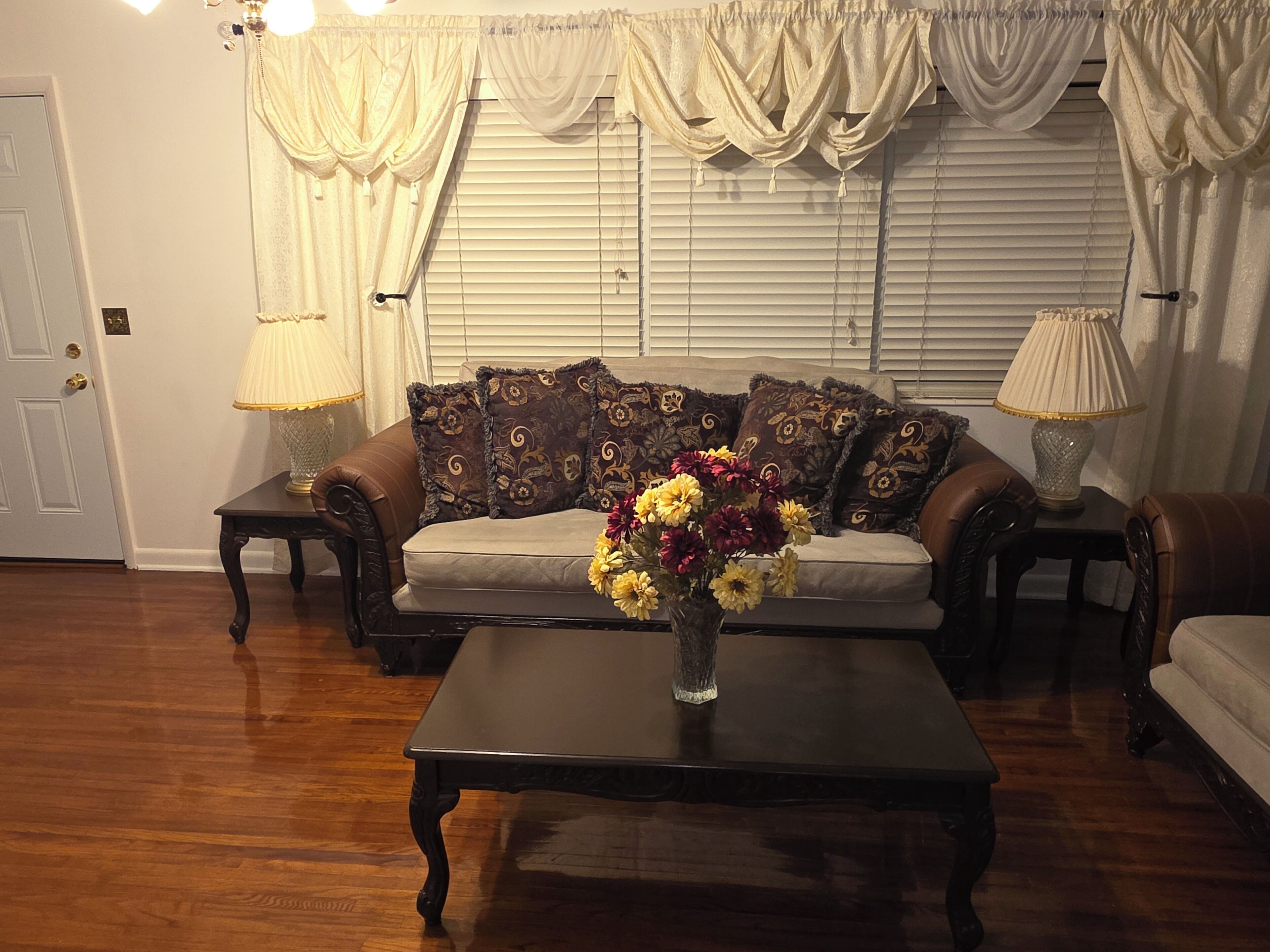 A living room with a sofa, a coffee table with a vase of flowers, and two lamps on side tables.