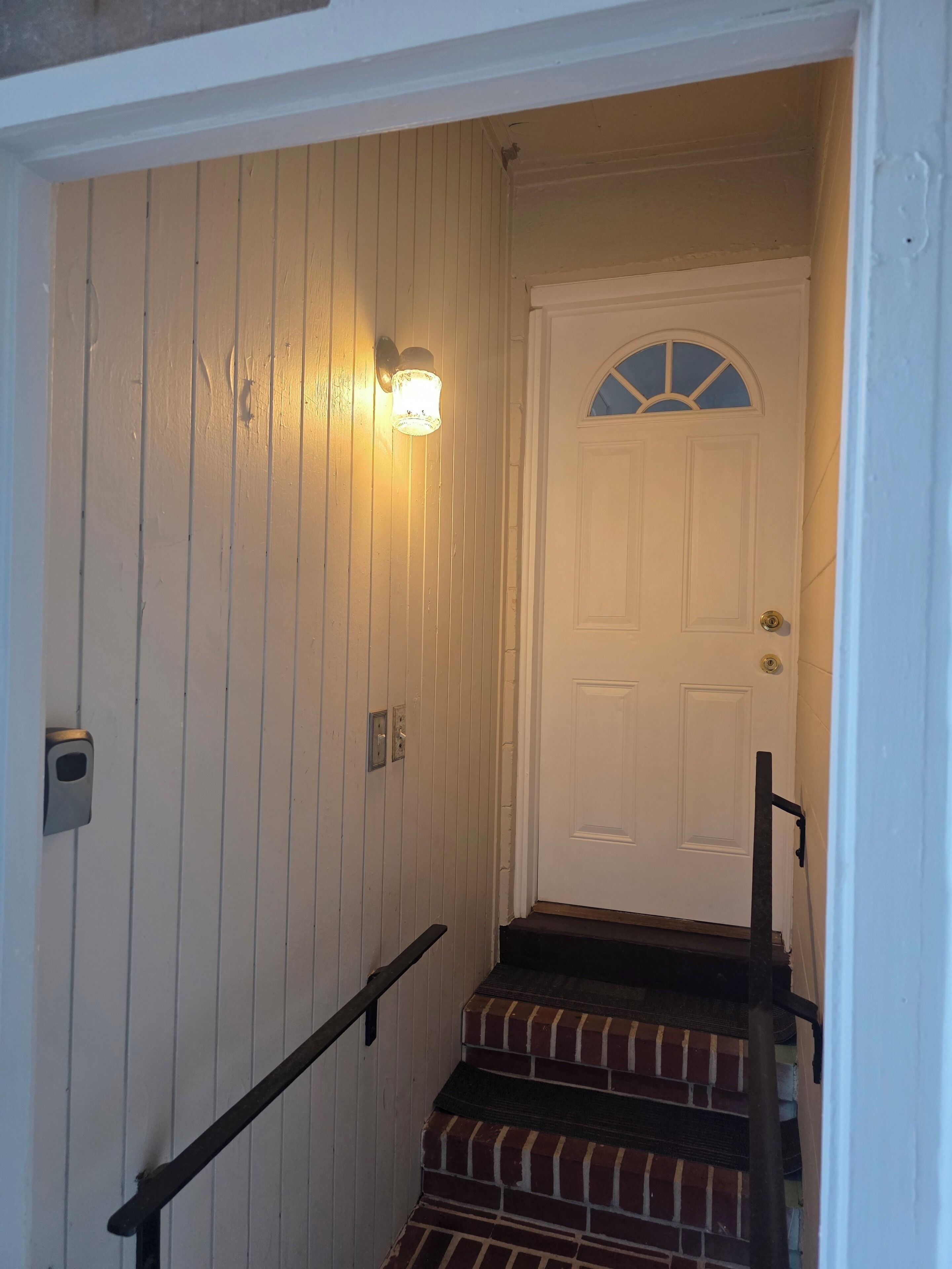 A staircase with a handrail, a white door with a window, and a wall-mounted light fixture.