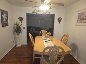 Una sala da pranzo con tavolo in legno, sedie, ventilatore a soffitto e decorazioni a parete.