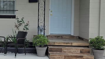 A house with a white door, a porch with steps, and two potted plants.