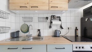 A modern kitchen with wooden cabinets, a stainless steel sink, a kettle, and a stove.