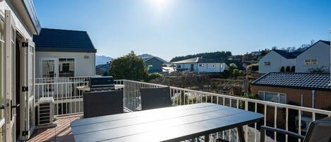 A balcony with a table and chairs, a grill, and a view of houses and mountains.