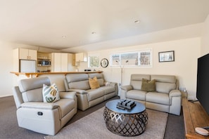 Ein Wohnzimmer mit zwei Sofas, einem Couchtisch, einem Fernseher und einer Küchenzeile im Hintergrund.