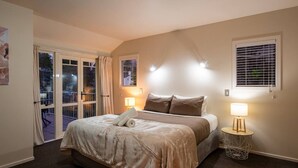 A bedroom with a bed, two bedside lamps, a window with blinds, and a door leading to a balcony. - Central Wanaka 3BR Apartment – Walk to Lake & Town (Wānaka)