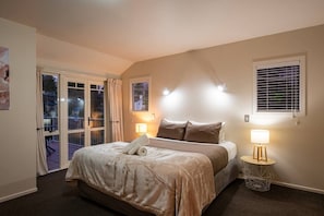 Ein Schlafzimmer mit einem Bett, zwei Nachttischlampen, einem Fenster mit Jalousien und einer Tür, die auf einen Balkon führt.