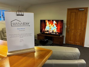 Ein Zimmer mit Fernseher, der einen Kamin zeigt, einem Holztisch, einer Couch und einer Tür.