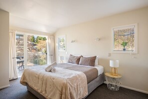 Un dormitorio con cama, una mesita de noche con lámpara, una ventana con planta y un balcón con cortinas.