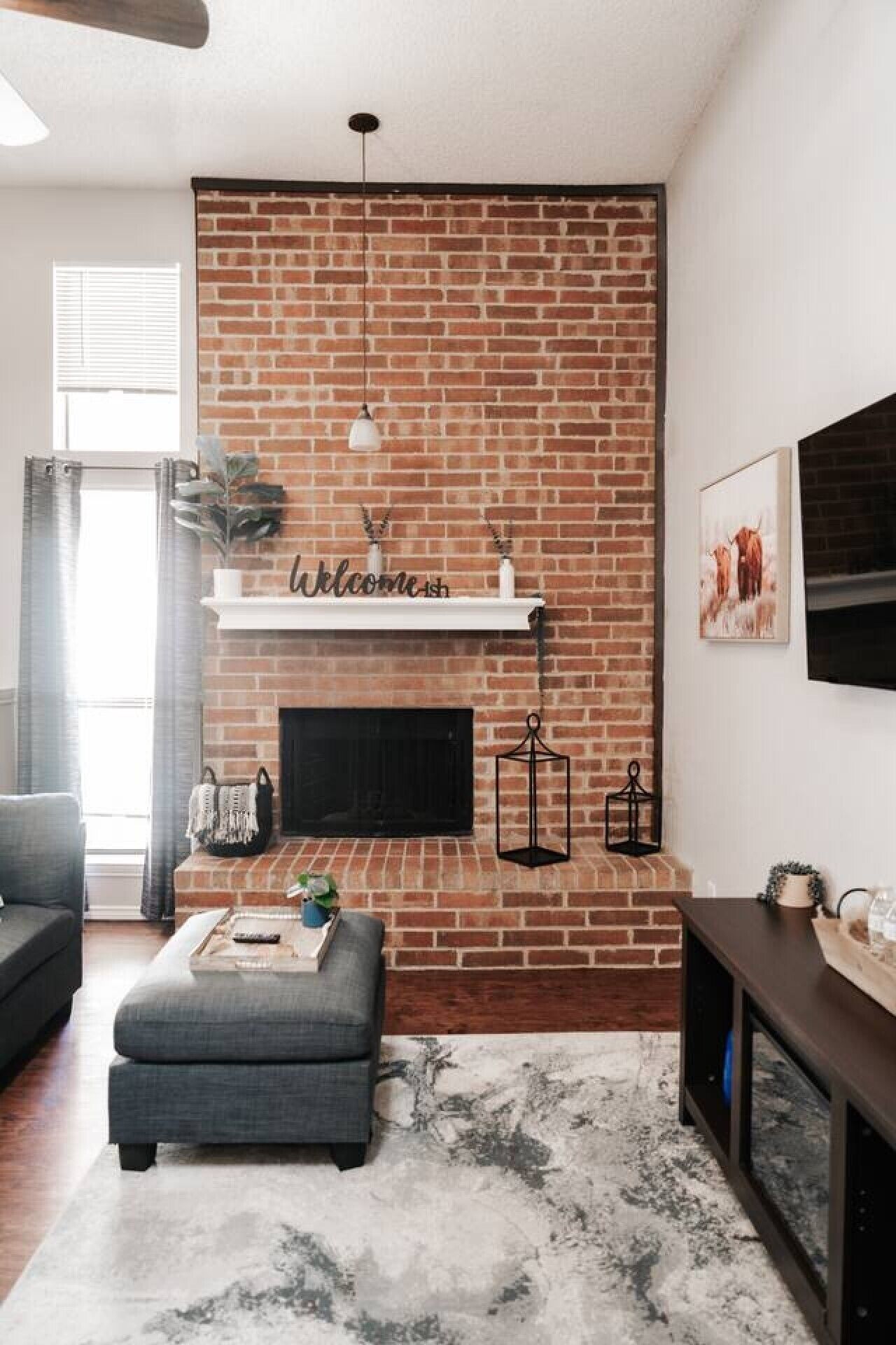 A living room with a brick fireplace, a mounted TV, and a 'Welcome' sign above it.
