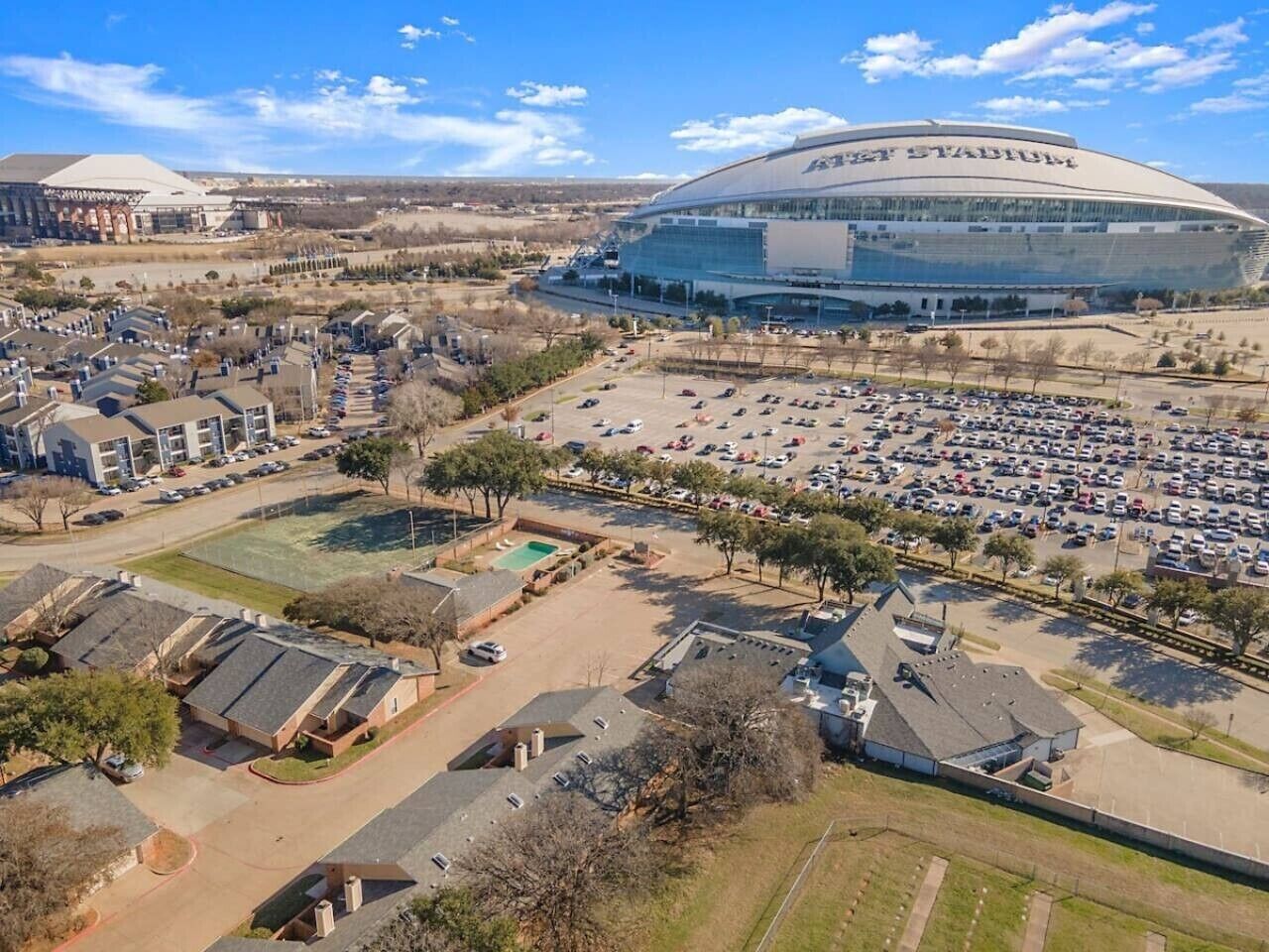 A stadium with a large parking lot, a swimming pool, and residential buildings.