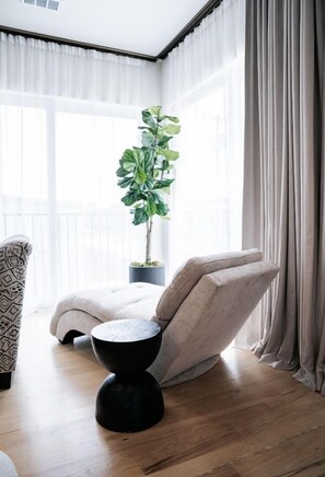Ein modernes Wohnzimmer mit großem Fenster, einem Topf mit Pflanze, einem Sofa und einem schwarzen Couchtisch.