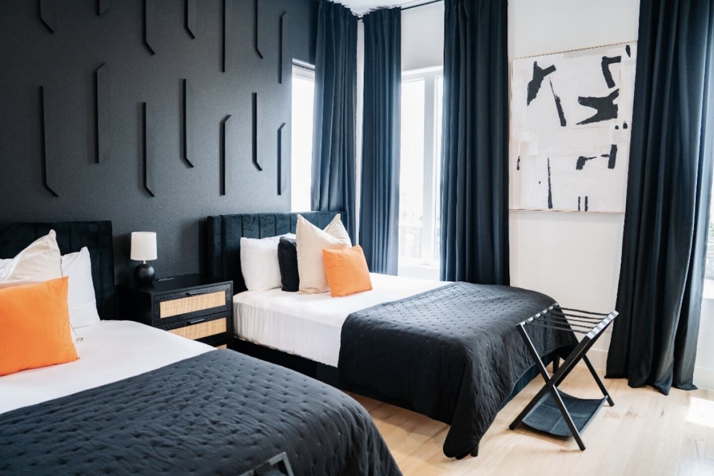Una habitación de hotel moderna con dos camas, una mesita de noche, una lámpara y un ventanal con cortinas.