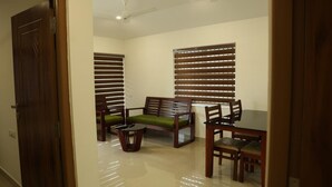 A room with a dining table, two chairs, a sofa, and a ceiling fan.