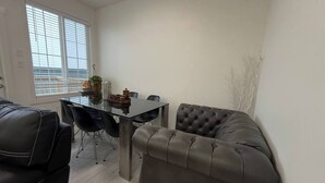 A modern living room with a glass dining table, black chairs, a grey sofa, and a large window with blinds. - Room-elegant Private Room With En-suite (Edmonton)