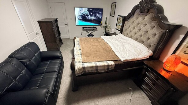 A bedroom with a bed, a black leather couch, a television, and a nightstand with a lamp. - Room-elegant Private Room With En-suite (Edmonton)