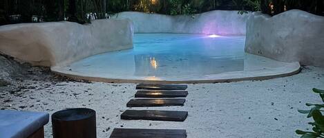 A pool area with a sandy path leading to the water, surrounded by greenery.