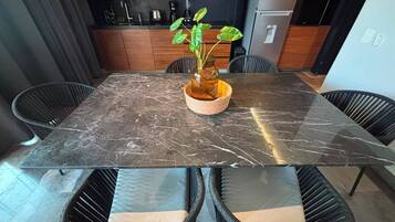 Un comedor con una mesa de mármol, sillas de mimbre y una planta en maceta.