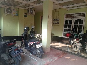 Un estacionamiento de motocicletas con varias motos, un ventilador de techo y paneles eléctricos en la pared.