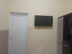 Ein Zimmer mit weißer Tür, einem an der Wand befestigten Flachbildfernseher und einem Schrank mit Spiegel.