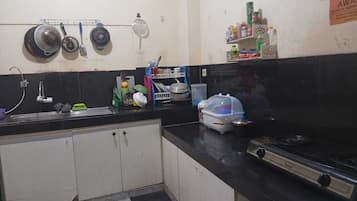 A kitchen with a black countertop, a stove, a sink, and a shelf with various items.