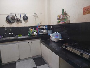 Una cocina con encimera negra, estufa, pileta y una alacena con diversos objetos.
