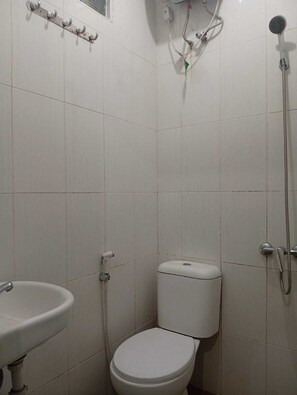 Une petite salle de bain carrelée, équipée de toilettes, d’un lavabo et d’une douche.
