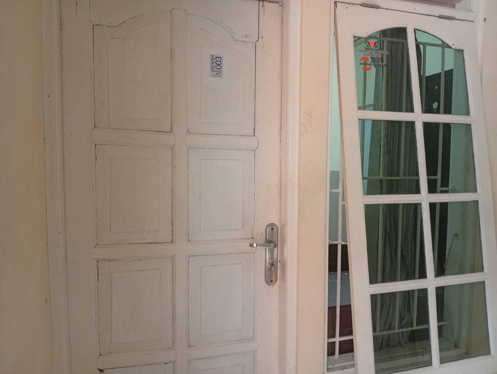 A white door with a room number sticker, a door handle, and a window with curtains.