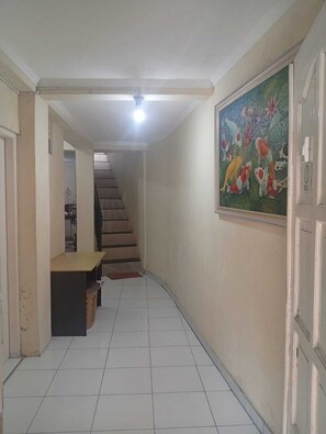 Un couloir avec un sol carrelé, un escalier, un tableau accroché au mur et une porte dotée d’une sonnette.