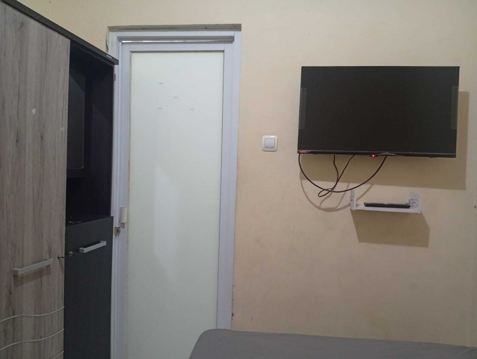 Una habitación con una puerta cerrada, un televisor montado y un enchufe en la pared.