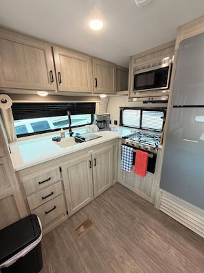 A compact RV kitchen with wooden cabinets, a microwave, a stove, and a refrigerator.