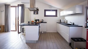 Une cuisine moderne avec des meubles blancs, un îlot central, un four encastré et une fenêtre au-dessus de l’évier.