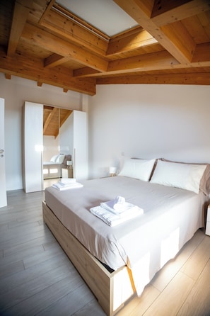 Ein Schlafzimmer mit Holzboden, einem großen Bett, einem Nachttisch und einem Spiegel.