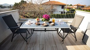 Un balcon avec une table mise pour le petit-déjeuner, comprenant des assiettes, un vase avec des fleurs et un verre de jus d’orange.