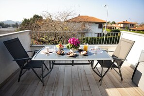 Ein Balkon mit einem für das Frühstück gedeckten Tisch, darunter Teller, eine Vase mit Blumen und ein Glas Orangensaft.