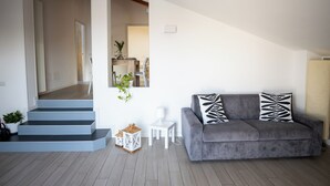 Un salon moderne avec un canapé gris, une table d’appoint blanche et un escalier menant à une autre pièce.