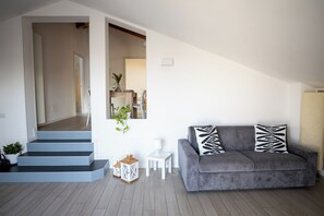 Ein modernes Wohnzimmer mit einem grauen Sofa, einem weißen Beistelltisch und einer Treppe, die in ein weiteres Zimmer führt.