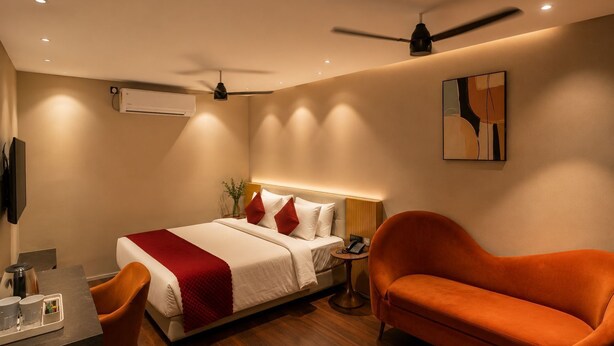 Habitación de hotel con cama, escritorio, silla, sofá, ventilador de techo, aire acondicionado y un cuadro en la pared.