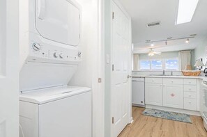 A laundry room with a washing machine and dryer, a kitchen with white cabinets, a window with curtains, and a ceiling fan. - 2/2 Ocean front/view, heated pool, snowbird ready (Fort Walton Beach)